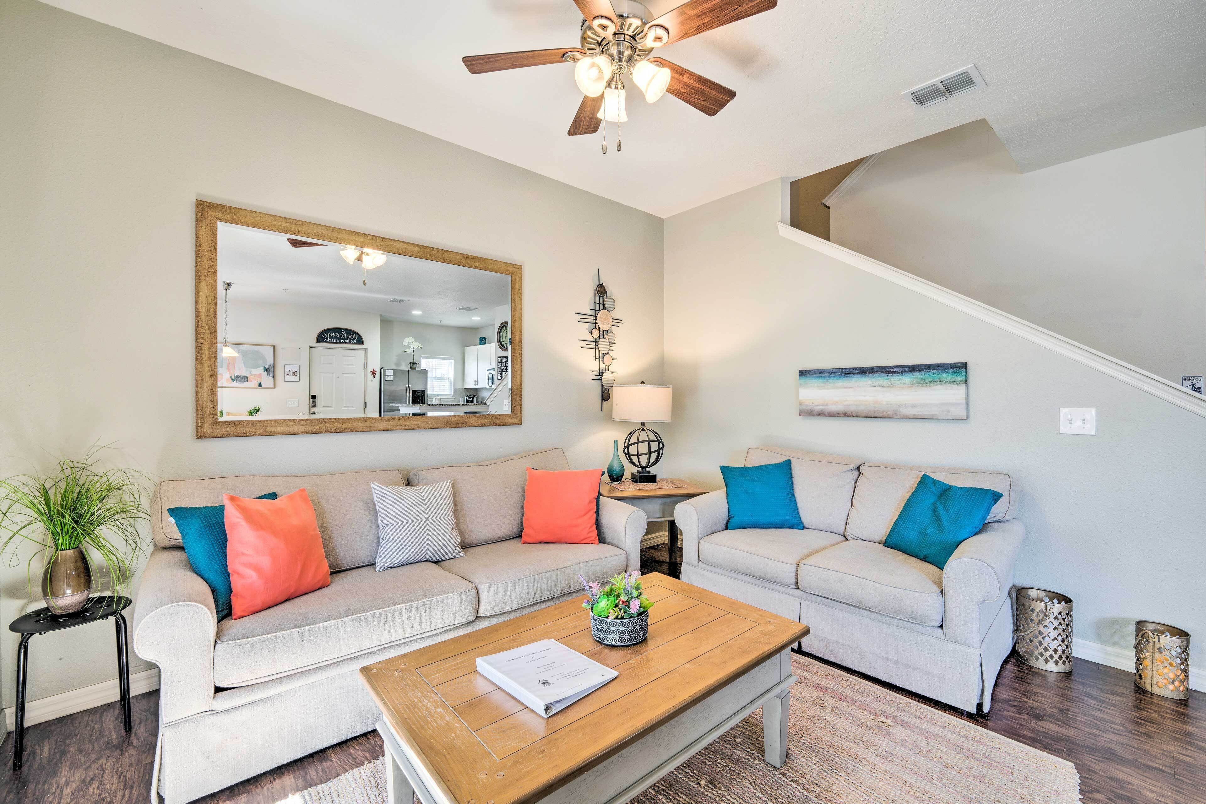 A living room with two light-colored sofas, a wooden coffee table, a ceiling fan, a mirror, and a staircase.