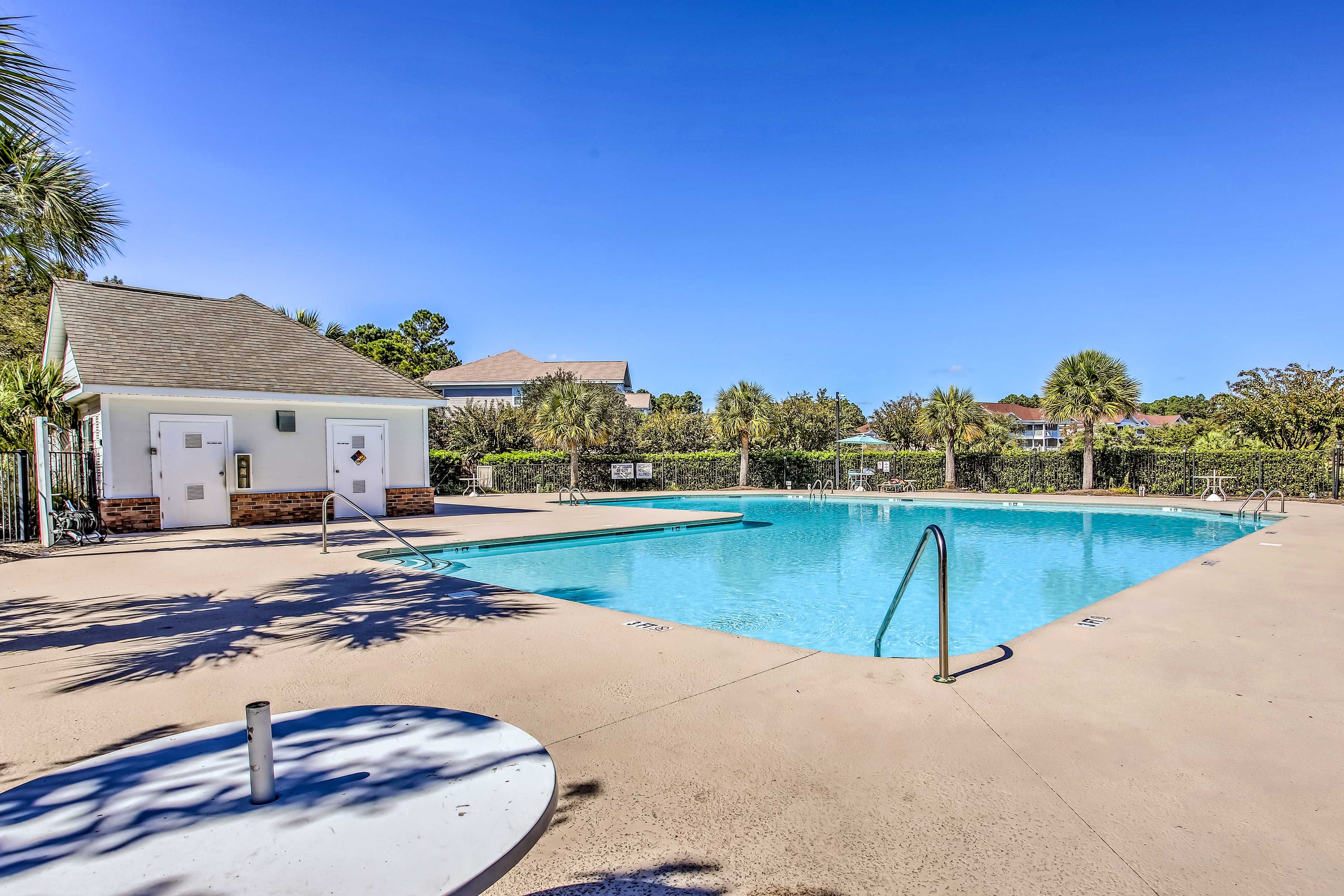 A swimming pool with a lifeguard stand, a covered seating area, and a building with a tiled roof.