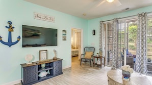 A room with a TV, a console table, a chair, and a view through a window. - Fall Retreat at Barefoot Resort 1st Floor (North Myrtle Beach)