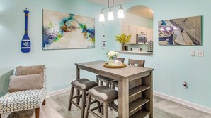 A dining area with a wooden table, two chairs, a blue paddle, and abstract art on the walls. - Fall Retreat at Barefoot Resort 1st Floor (North Myrtle Beach)