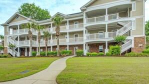 A multi-story residential building with balconies, a central walkway, and a brick facade. - Fall Retreat at Barefoot Resort 1st Floor (North Myrtle Beach)