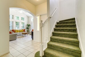 Un escalier dont les marches sont recouvertes d’une moquette verte et dont les balustrades sont blanches, menant à un palier avec une porte blanche.