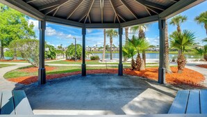 A gazebo with a concrete floor and a wooden roof, surrounded by palm trees and a water body. - Townhome in Berkeley Lake Resort, 9 Mi to Wdw! (Kissimmee)