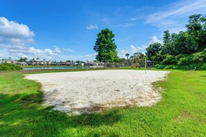 A sandy volleyball court with a net, surrounded by green grass and trees.