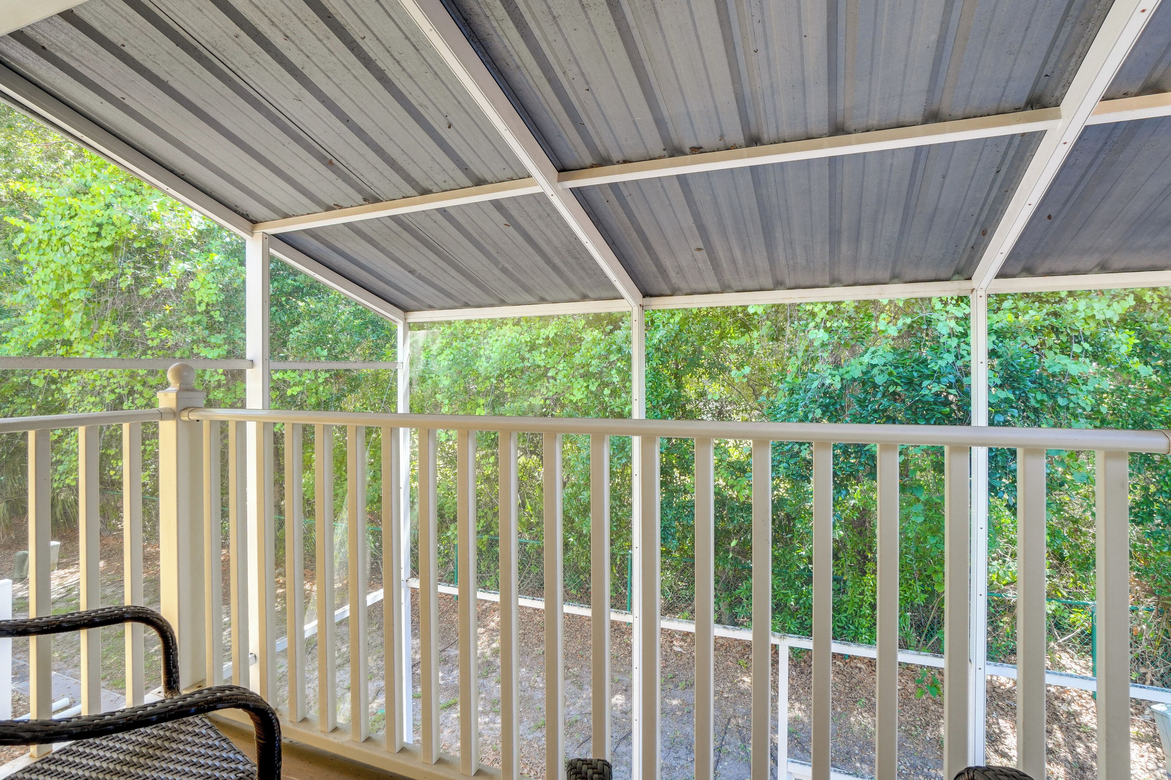 A covered outdoor area with a white railing, a wicker chair, and a view of greenery.