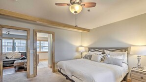 Ein Schlafzimmer mit einem großen Bett, Nachttischlampen, einem Deckenventilator und Blick auf einen anderen Raum durch eine offene Tür.