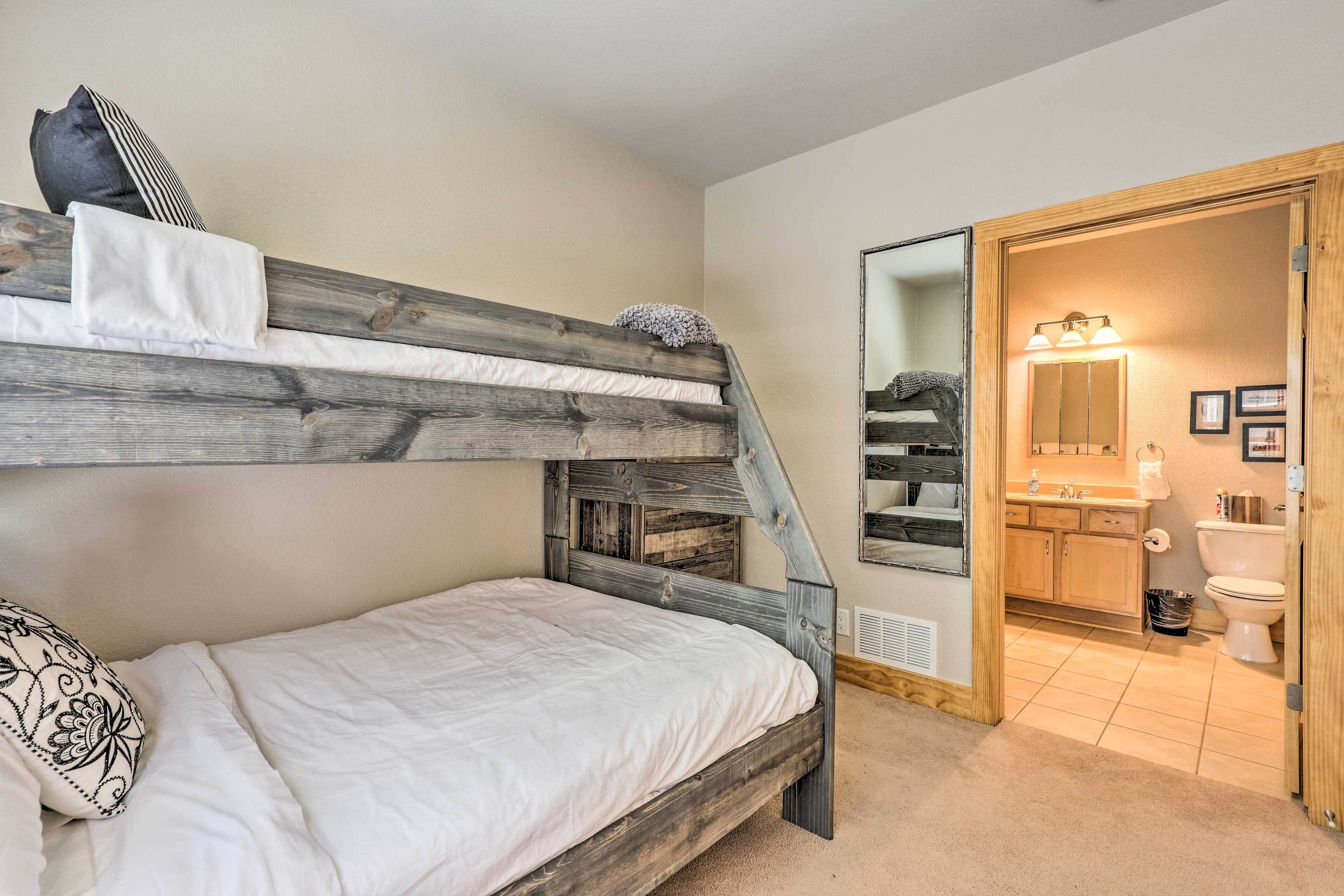 A bedroom with a bunk bed, a bedside table, a mirror, and a view into the bathroom.