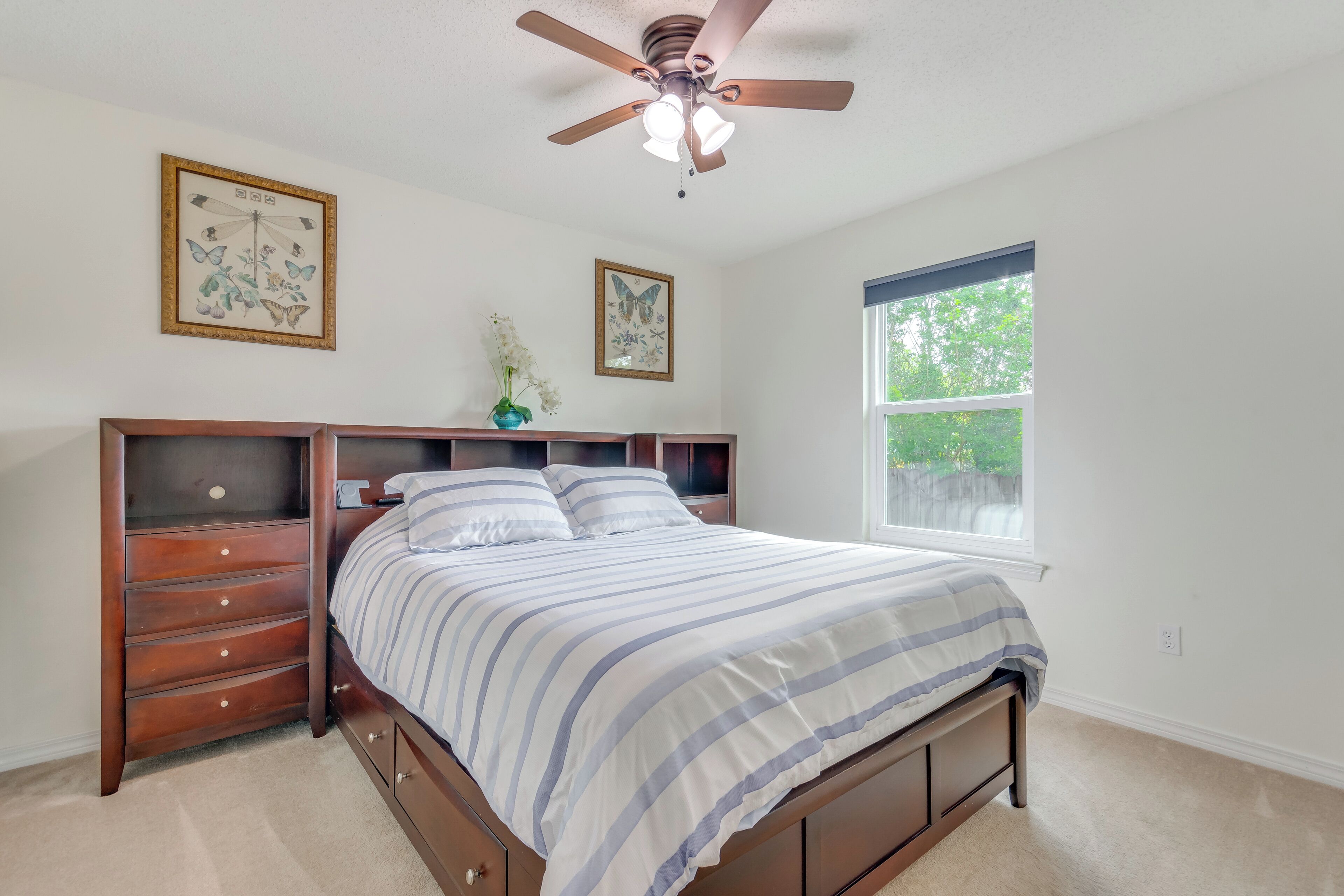 A bedroom with a bed, wooden dresser, ceiling fan, and two framed pictures on the wall.