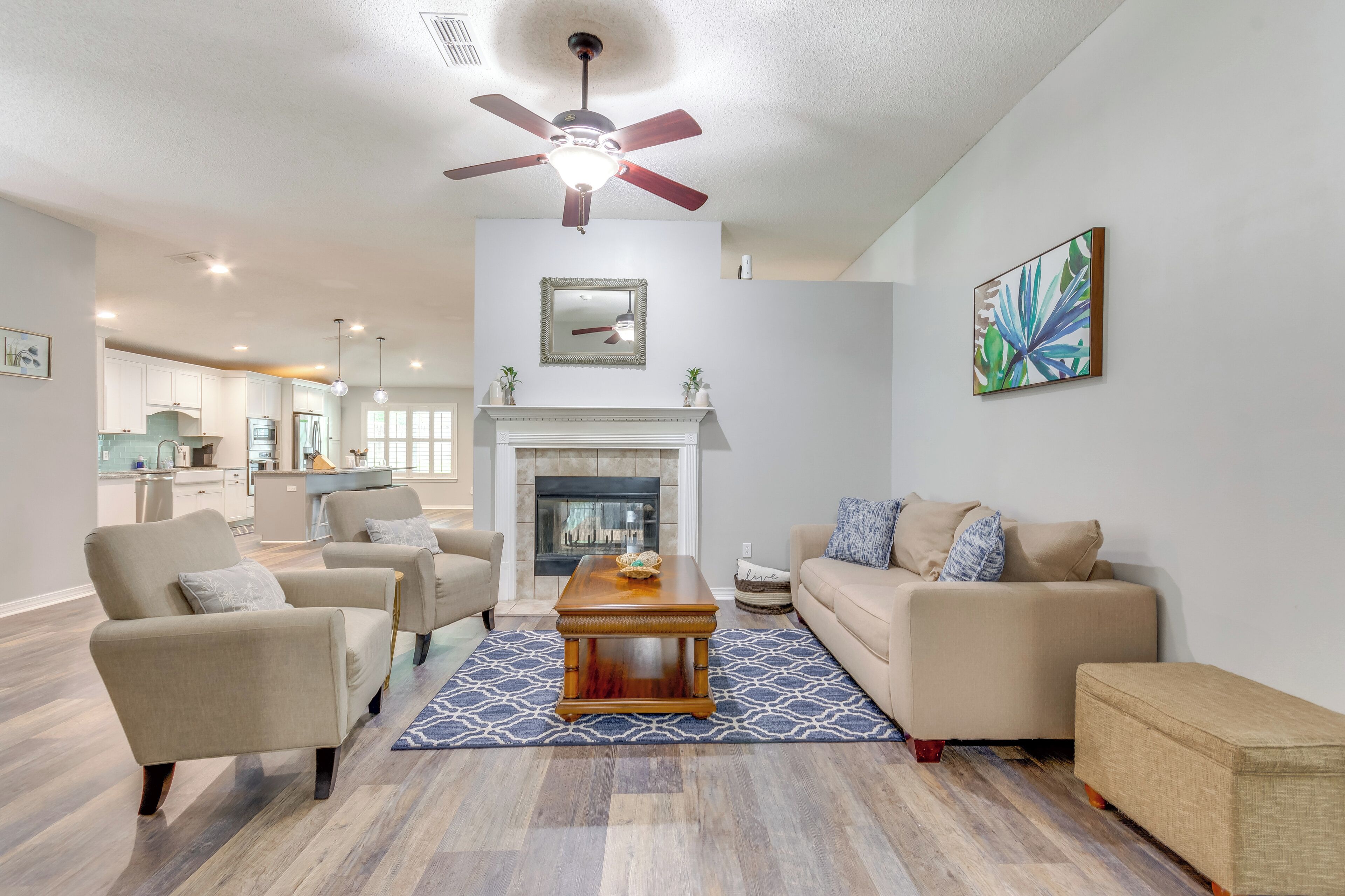 A modern living room with a fireplace, a ceiling fan, and a dining area in the background.