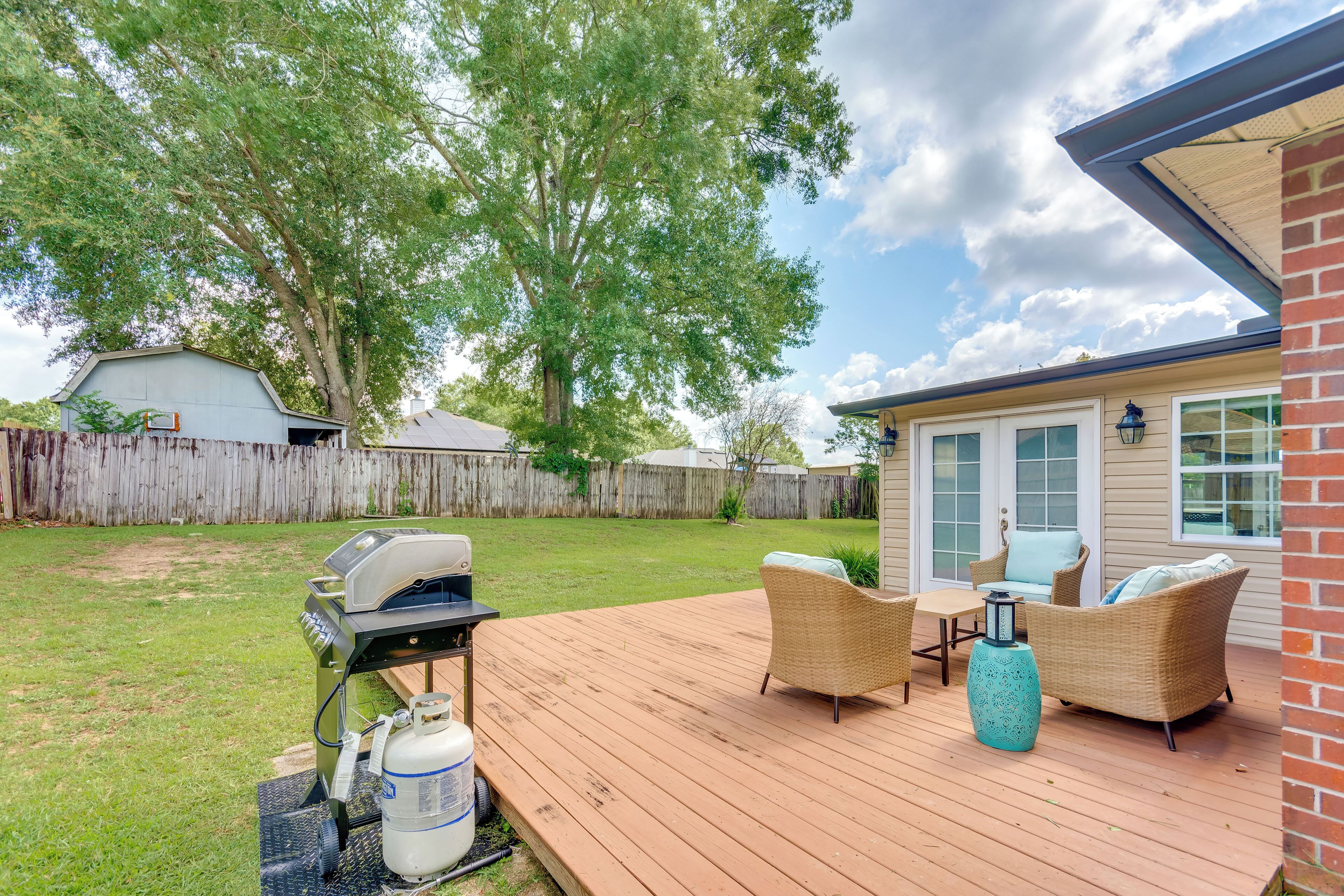 Une terrasse en bois avec des meubles d’extérieur, un barbecue et une bouteille de propane.