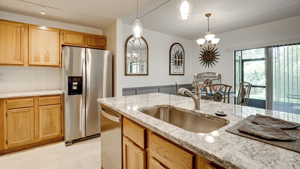 A modern kitchen with wooden cabinets, stainless steel appliances, a granite countertop, and pendant lighting.