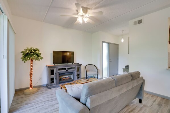 A modern living room with a grey sofa, a flat-screen TV, a fireplace, and a tall floor lamp. - St Augustine Condo w/ Screened Porch, Pool Access! (St. Augustine)
