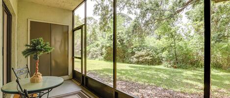 A room with a large window overlooking a garden. There is a table with chairs and a small potted plant.