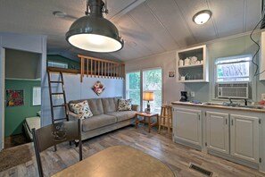 A compact living space with a sofa, a small table, a ladder, and a kitchenette area. - Cozy Middle Bass Cabin w/ Grill & Lagoon Access! (Put-in-Bay)