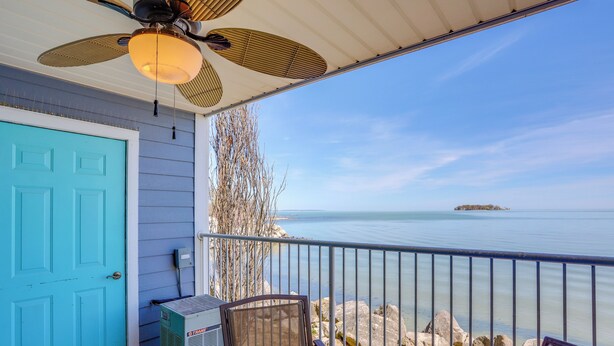 A balcony with a view of the sea, a blue door, and a ceiling fan. - Waterfront Middle Bass Condo w/ Pool Access! (Put-in-Bay)