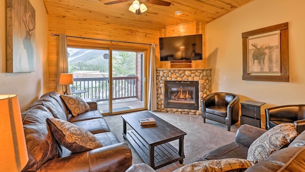 A cozy living room with a stone fireplace, leather sofas, a flat-screen TV, and a ceiling fan.