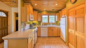 A kitchen with wooden cabinets, a white refrigerator, and a window with a view of trees.