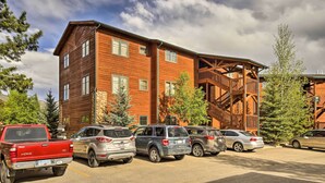 A multi-story building with a wooden exterior, a covered outdoor area with stairs, and a parking lot with several vehicles.