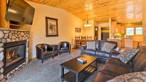 A cozy living room with a stone fireplace, leather furniture, and a television mounted on the wall.