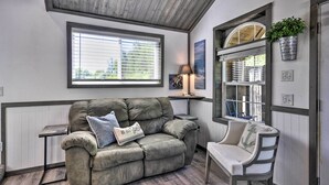 A cozy living room with a grey sofa, a small side table, a chair, and a window with blinds. - Floating Home on Columbia River w/ Provided Kayaks (Vancouver)
