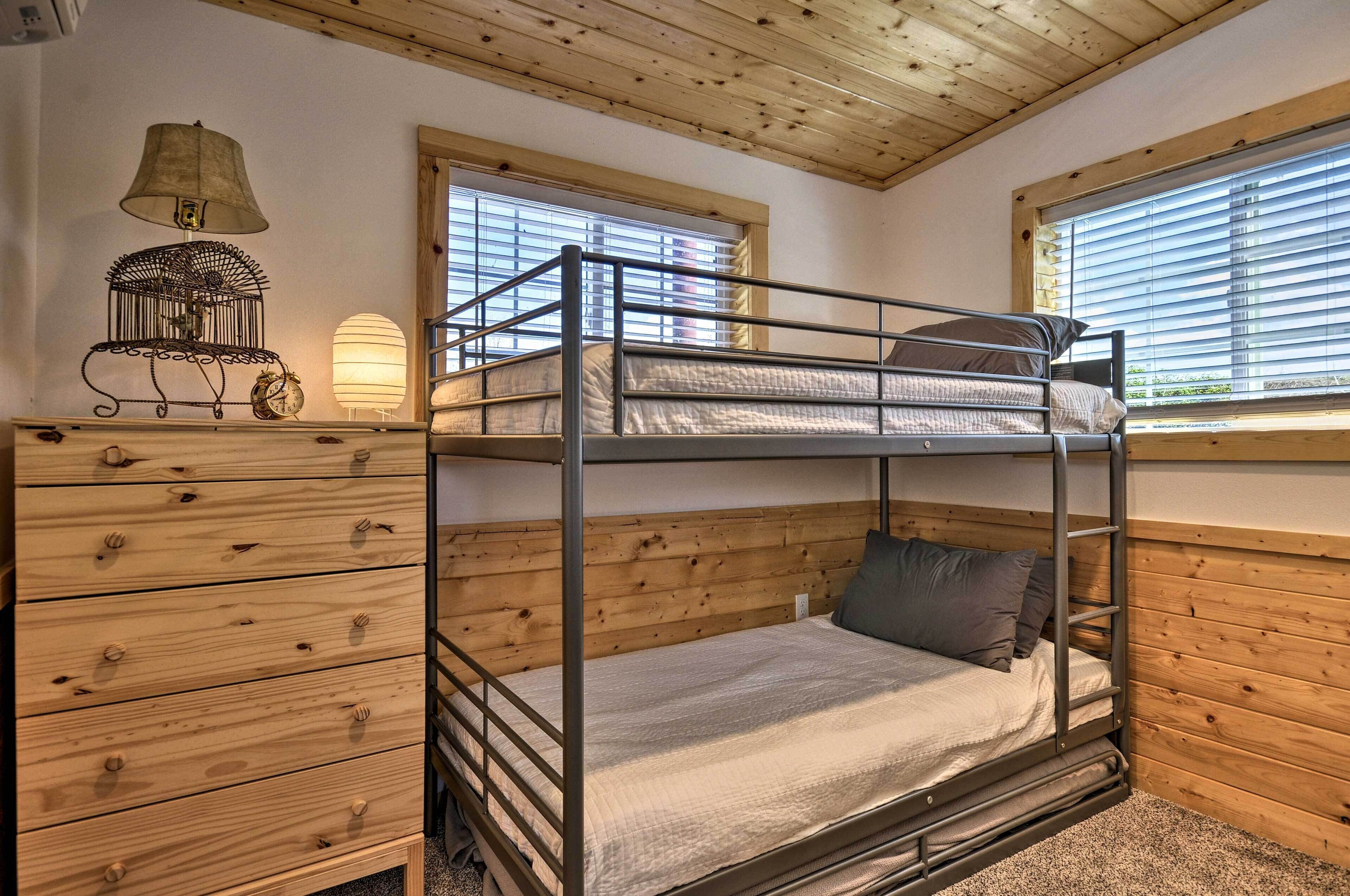 A bunk bed room with a wooden ceiling, a dresser with drawers, a lamp, and a window with blinds.