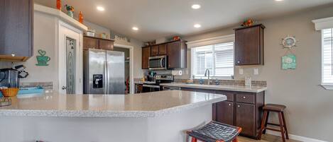 Una cocina con una isla grande, electrodomésticos de acero inoxidable, armarios de madera y una ventana con persianas.