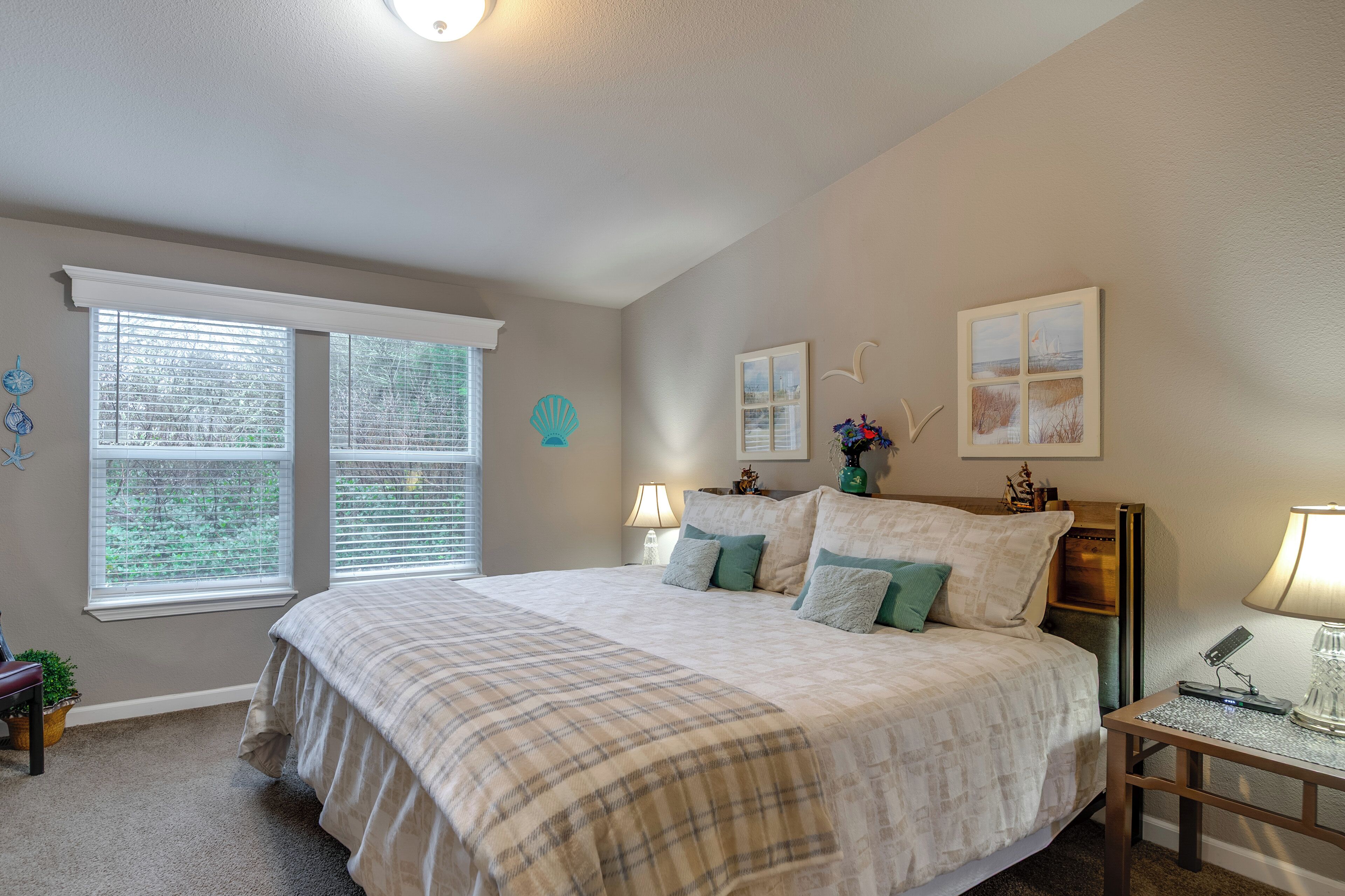 A bedroom with a large bed, two bedside tables, a nightstand, a window with blinds, and wall decorations.