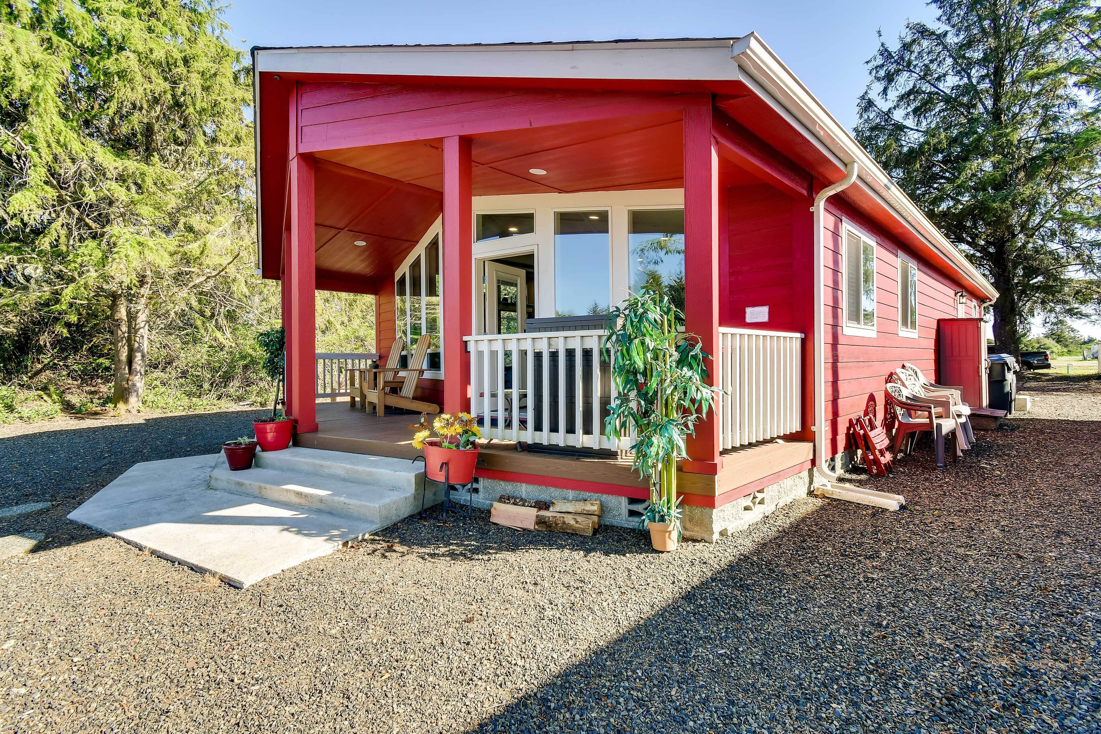 Ein rotes, eingeschossiges Haus mit verdeckter Veranda, einer Haustür und einem kleinen Vorgarten mit Kies und Pflanzkübeln.