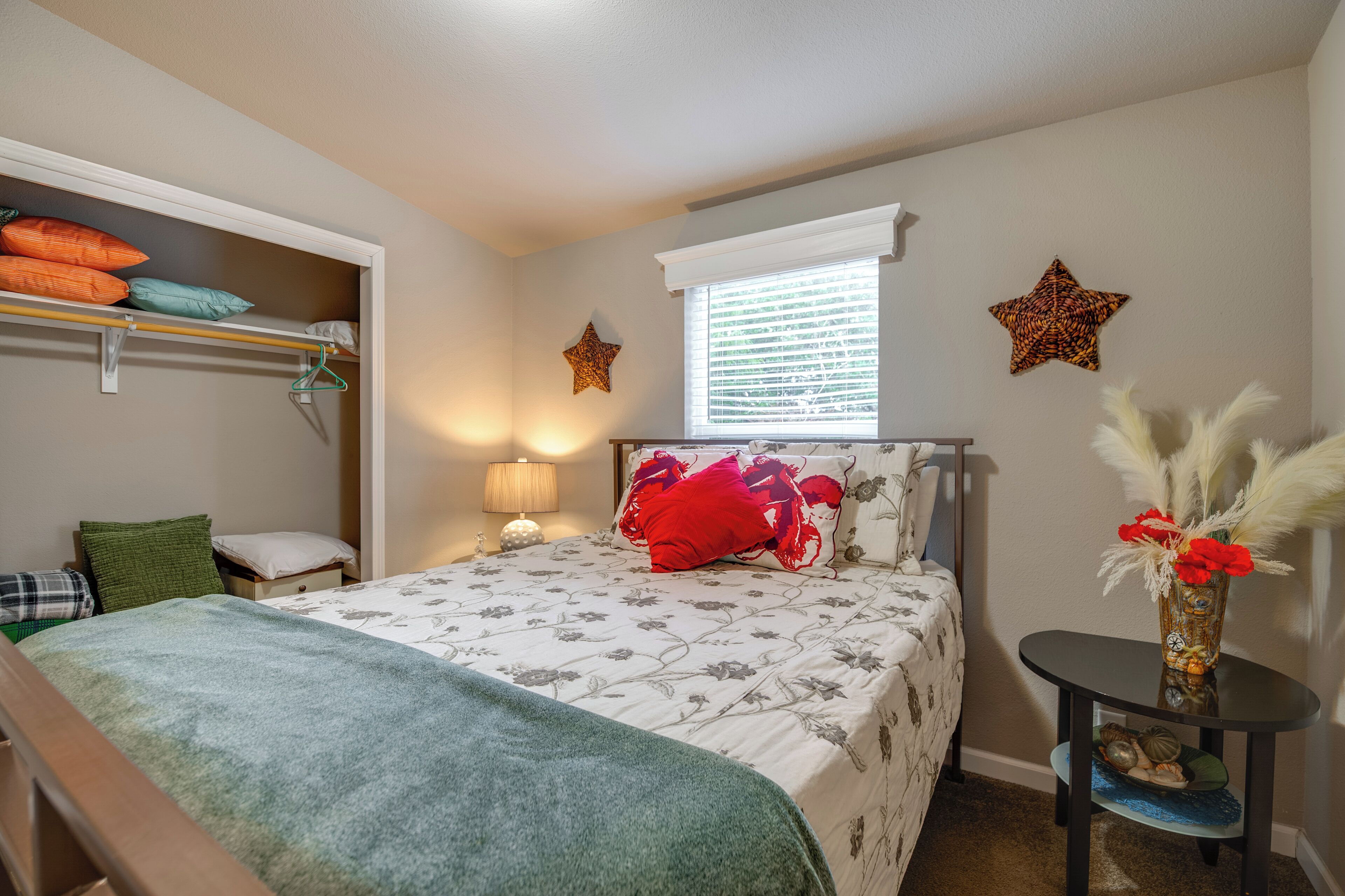 Quarto com cama, mesa de cabeceira, cômoda, janela com persianas e estrelas decorativas na parede.