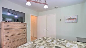 Ein Schlafzimmer mit einem hölzernen Schminktisch, einem Bett mit gemustertem Quilten, einem Flachbildfernseher, einer Deckenleuchte und einem Bild von Fischen an der Wand.