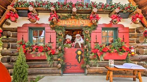 Une cabane en rondins sur laquelle est accrochée une pancarte indiquant « La maison du Père Noël », décorée d’ornements de Noël et de guirlandes.