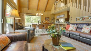 A cozy living room with leather sofas, a coffee table with books, and a staircase with a railing. - Lake Arrowhead Family Home w/ Game Room (Lake Arrowhead)