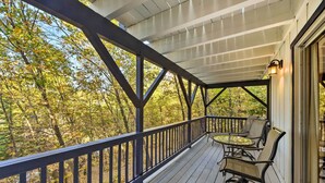 Une véranda couverte avec une balustrade, une table avec des chaises et une vue sur les arbres.