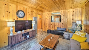 Una sala de estar con paneles de madera, un televisor, un sofá, una mesa de centro y un reloj en la pared.