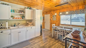 Cocina con paneles de madera, armarios blancos, un fregadero y una zona comedor con mesa y sillas.