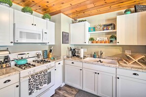 Une cuisine moderne avec des armoires blanches, un four à micro-ondes encastré, une cuisinière à gaz et un plan de travail en granit.