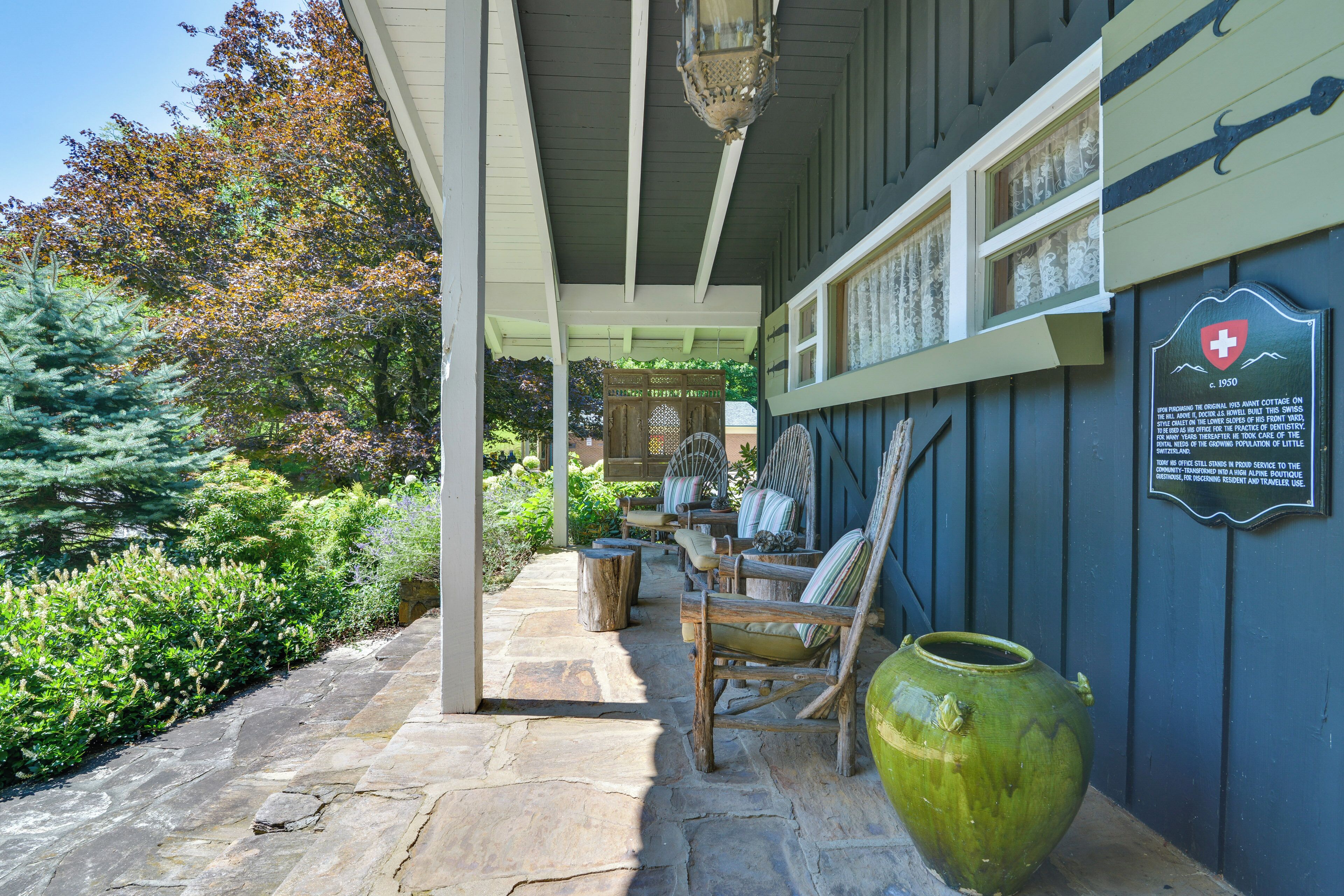 A covered outdoor area with stone flooring, wooden furniture, and a green vase.