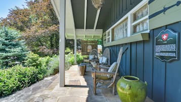A covered outdoor area with stone flooring, wooden furniture, and a green vase.