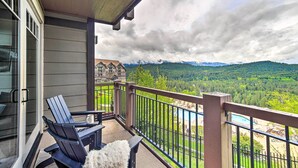 A balcony with two chairs and a table, overlooking a mountainous landscape and a swimming pool.