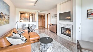 A modern living room with a leather sofa, a fireplace, a dining area, and a kitchen in the background.