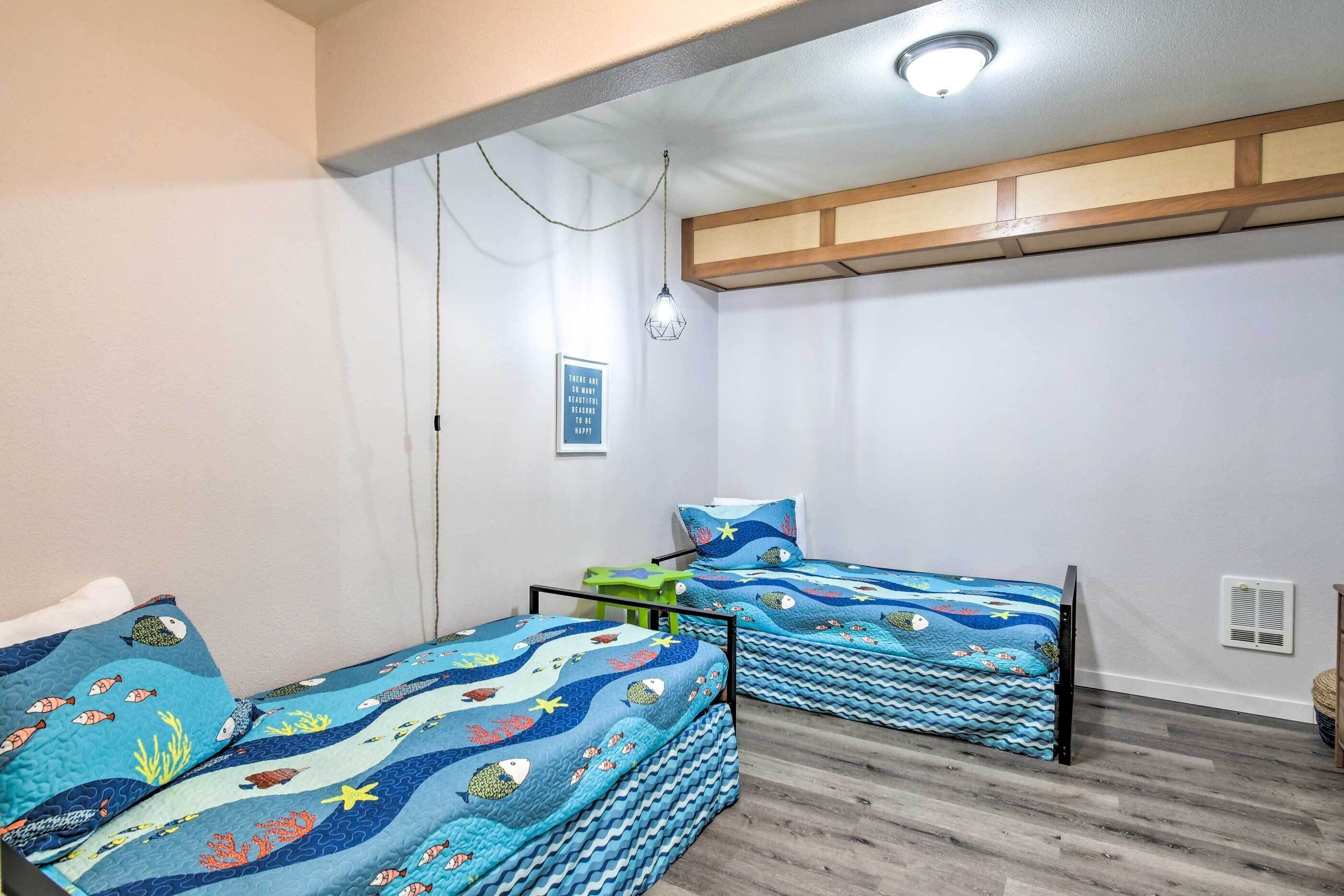 Un dormitorio con dos camas, cada una con una colcha azul con motivos marinos. Hay una lámpara en el techo y un calentador de pared.
