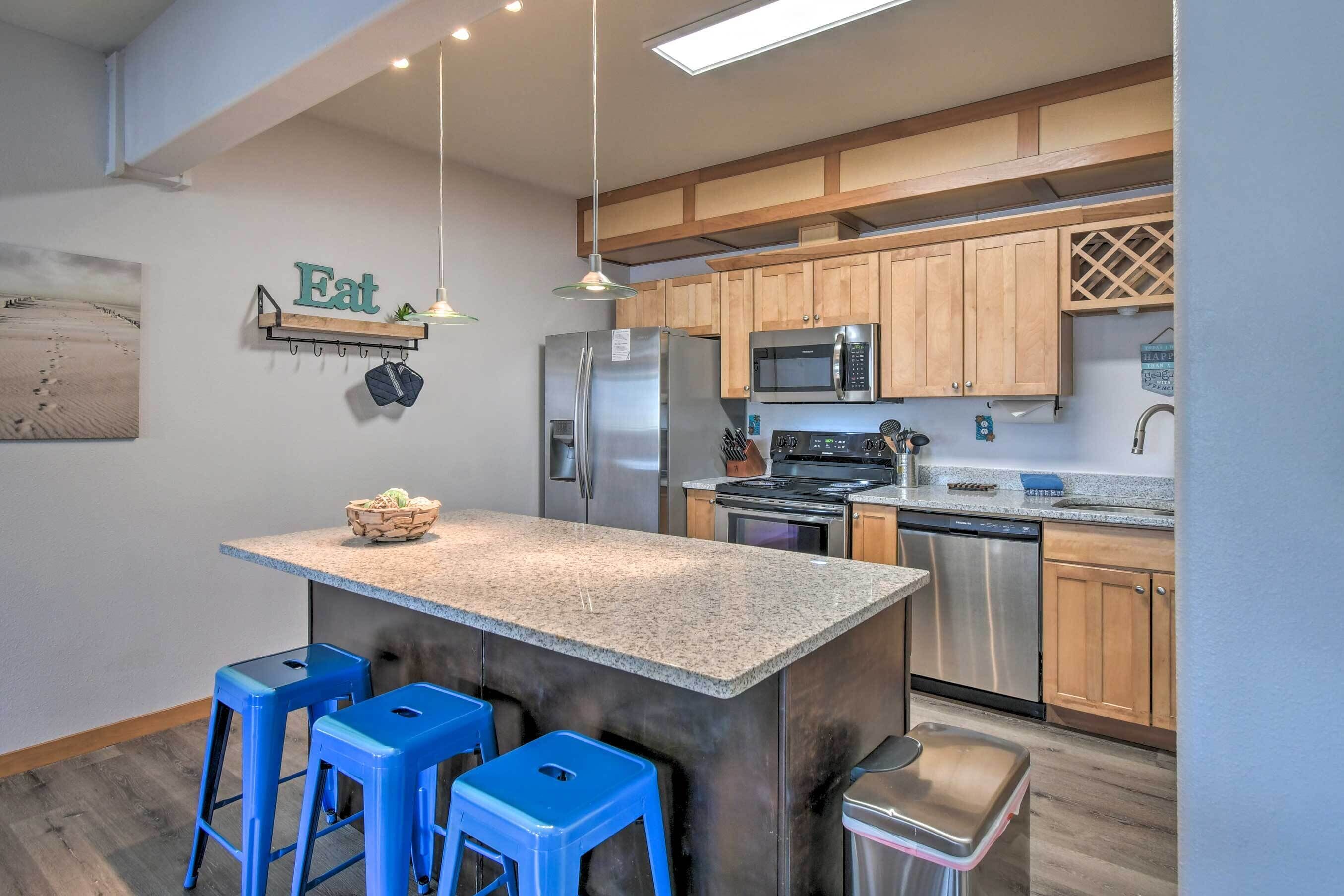 A modern kitchen with a central island, blue bar stools, stainless steel appliances, and wooden cabinets.