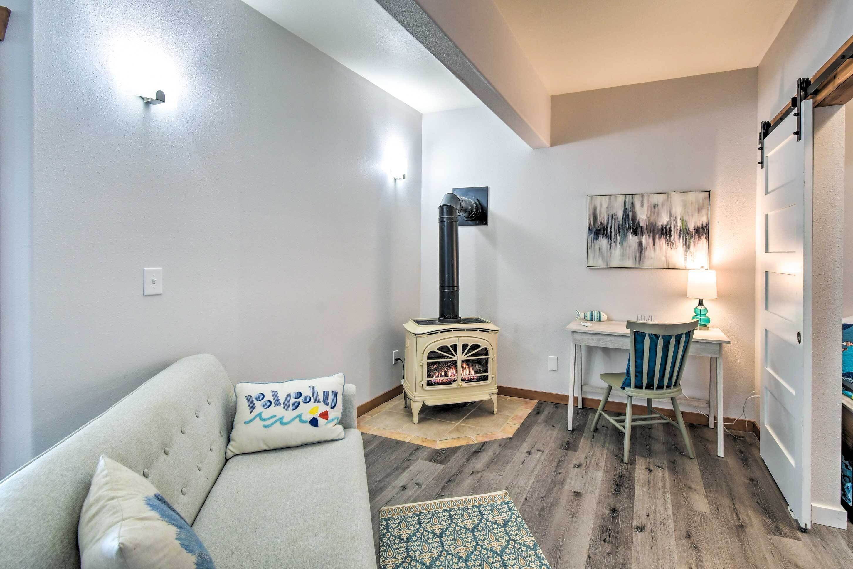 A cozy living room with a sofa, a small table, a chair, a wooden floor, a wall-mounted heater, and a painting.