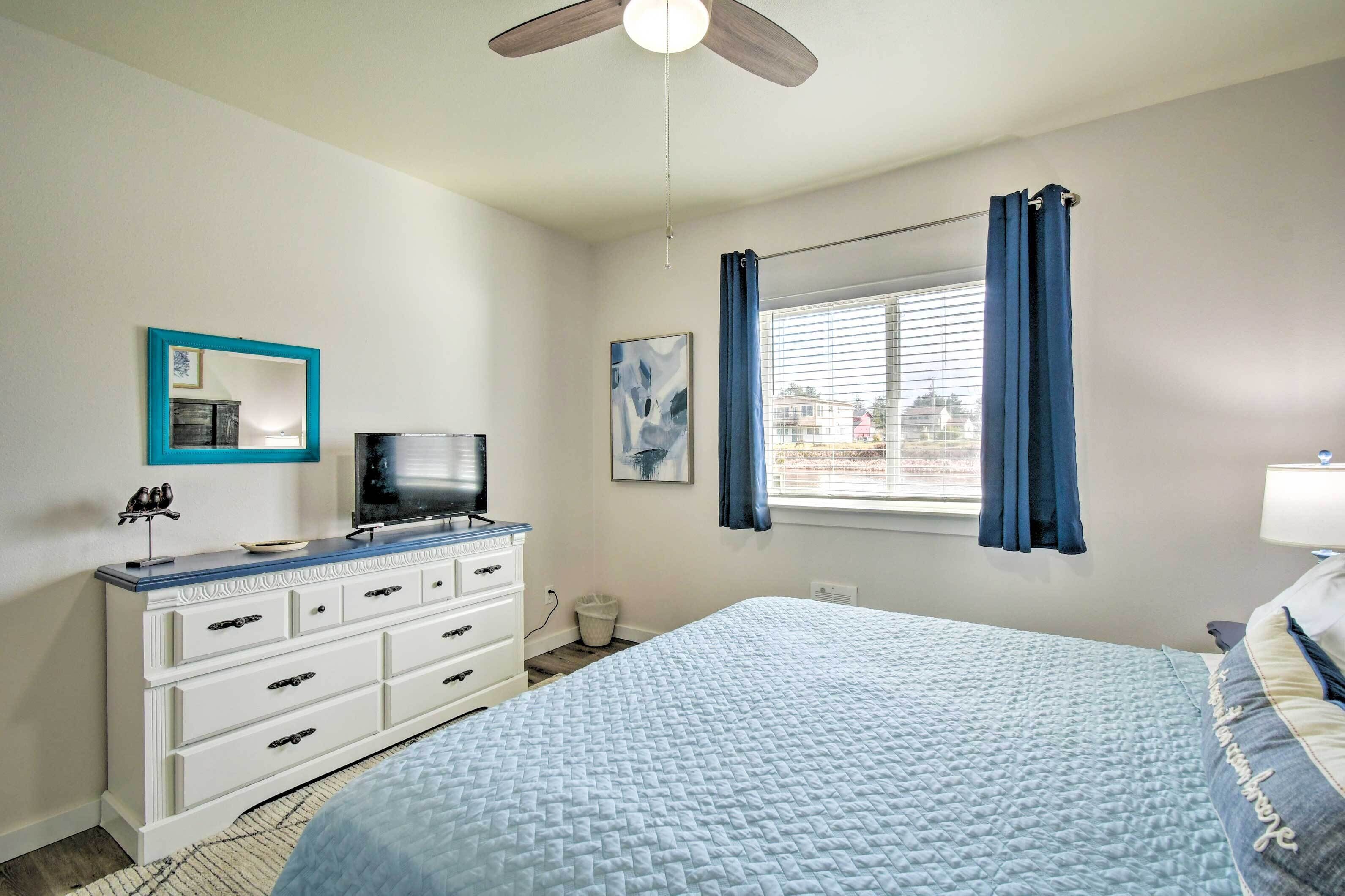 A bedroom with a bed, a dresser, a television, a window with curtains, and a ceiling fan.