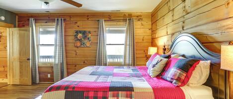 A wooden-paneled bedroom with a bed, curtains, a ceiling fan, and a window.