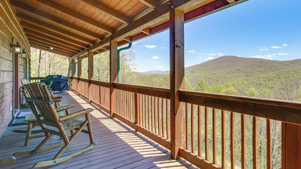 A wooden deck with rocking chairs, a grill, and a view of a forested mountain.