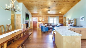 A spacious living area with a wooden ceiling, a dining table, blue chairs, and a kitchen with a granite countertop.