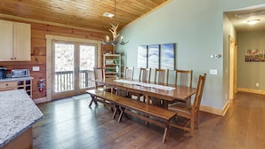 A spacious dining area with a wooden table and benches, a kitchen with wooden cabinets, and a chandelier.