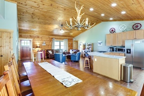 A spacious living area with a wooden ceiling, a chandelier, a dining table with chairs, and a kitchen area with a refrigerator and microwave. - Family Cabin w/ Private Hot Tub & Views in Boone! (Boone)
