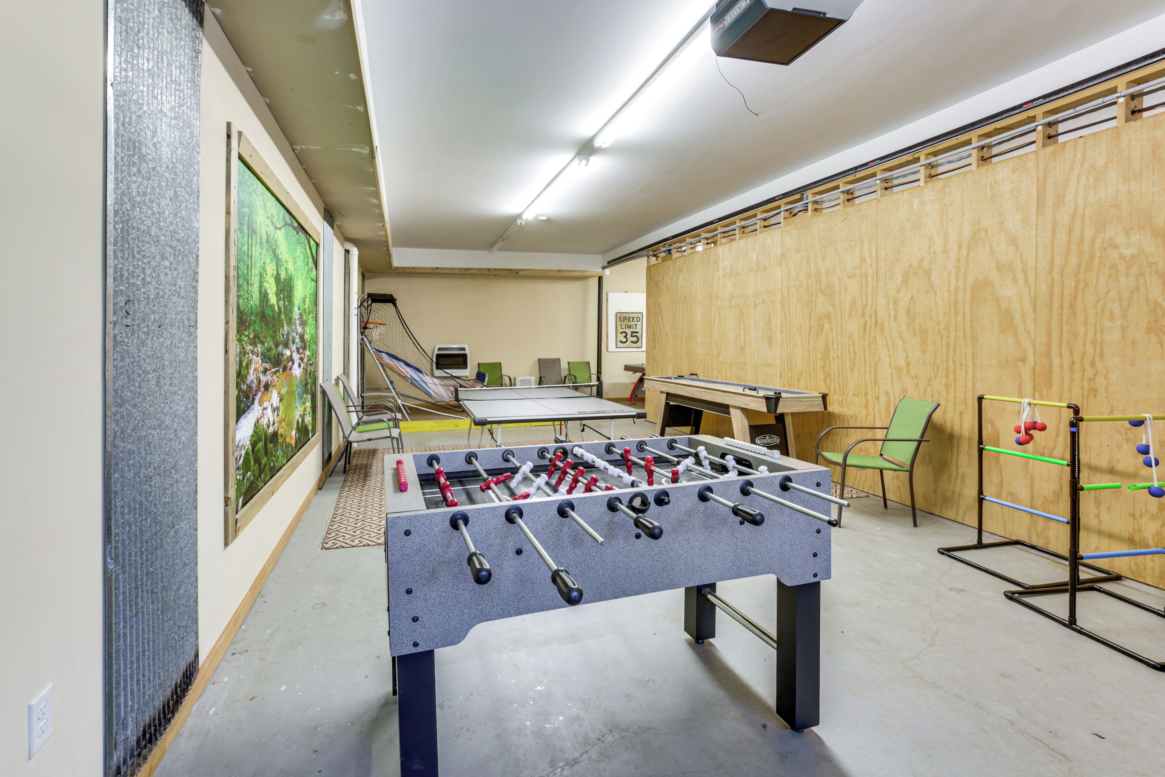 A room with a foosball table, a ping pong table, and a green chair.